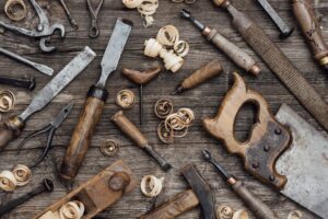 An assortment of vintage woodworking tools spread out on a rustic wooden surface made from recycled pallets, including saws, chisels, and planers with wood shavings.