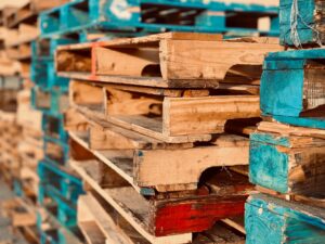 Stacks of colorful wooden pallets piled up, showcasing aged wood and traces of blue and red paint, are arranged about the warehouse.
