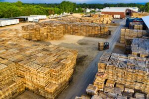 Aerial view of an industrial lumber yard with stacks of wooden planks and a forklift moving pallets of materials.