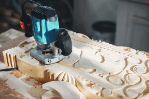 Electric hand router on a detailed wooden carving project using recycled pallets in a workshop.