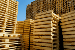 Stacks of wooden pallets, ready for transport, bask under a clear blue sky, showcasing the efficiency and reliability of our services.