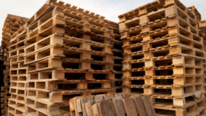 Stacks of wooden pallets are arranged outdoors, with some pallets leaning against the piles under a partly cloudy sky.