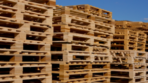 Stacks of custom pallets are arranged in large, organized piles outdoors under a clear blue sky.