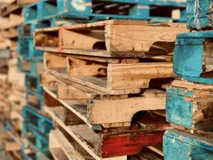 A close-up view of a stack of wooden pallets, some painted blue and others unpainted, arranged in rows outdoors invites the question: what is the best type of pallet to buy for your needs?.