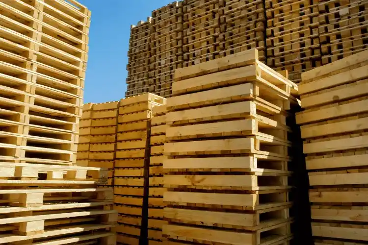 Tall stacks of wooden pallets, supplied by a leading Pallet Company in Surrey, are arranged outdoors under a clear blue sky.