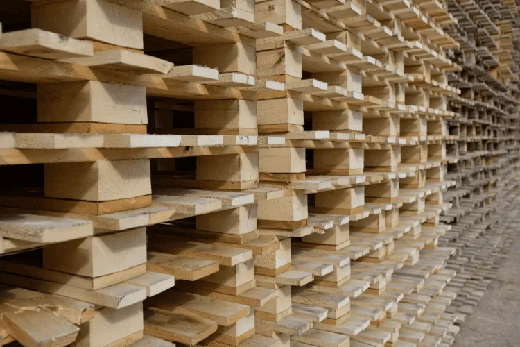 A large stack of wooden pallets is arranged in rows, viewed from the side inside a warehouse or storage area of a leading Pallet Company in Surrey.