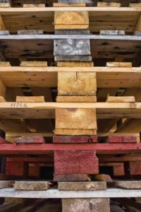 Stacked wooden pallets viewed from the front, showing various wood textures and colors, including natural and red-stained boards. These pallets may undergo a process for heat-treating pallets, enhancing their durability and meeting international shipping standards.