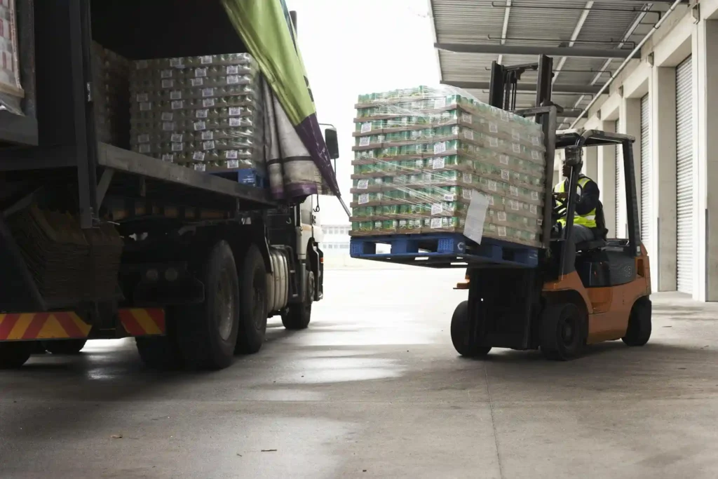A forklift operator unloads a shrink-wrapped pallet of goods from a truck at a warehouse loading dock, ensuring each delivery from the Pallet Company in Surrey is handled with efficiency and care.