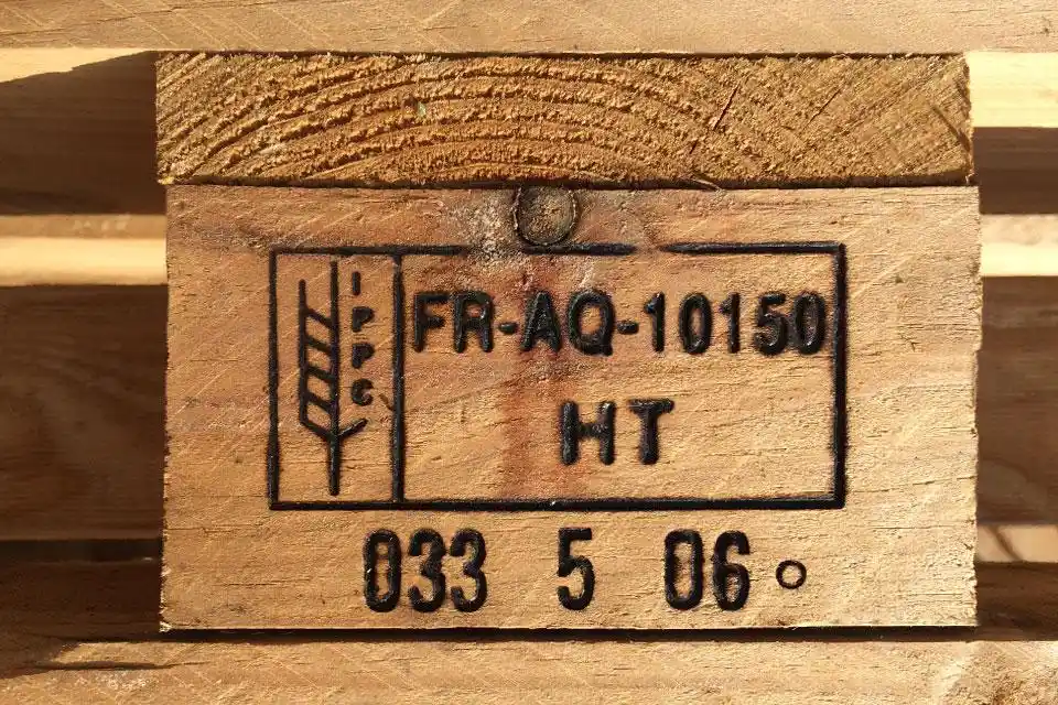 Close-up of a wooden pallet from a leading Pallet Company in Surrey, featuring a stamp with the IPPC logo, “FR-AQ-10150,” “HT,” and other identification numbers burned into the wood.