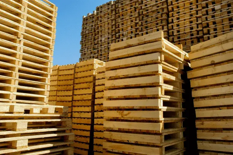 Stacks of wooden shipping pallets outdoors against a clear blue sky.