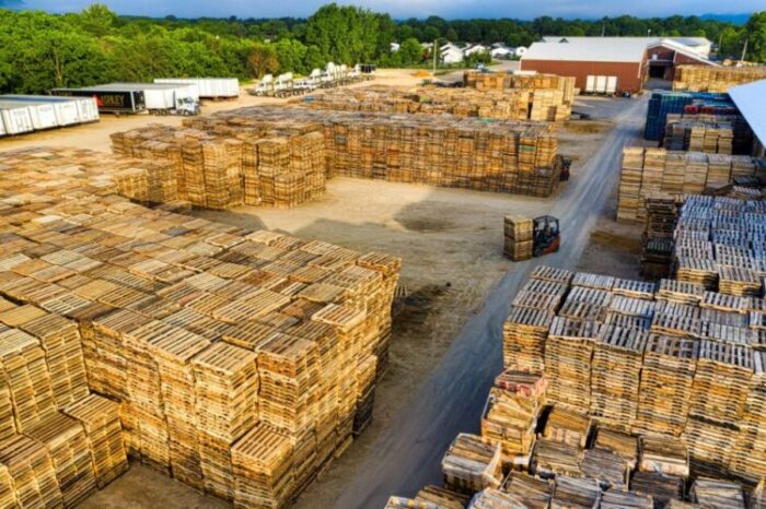 Aerial view of an industrial lumber yard with stacks of wooden planks and a forklift moving pallets of materials.